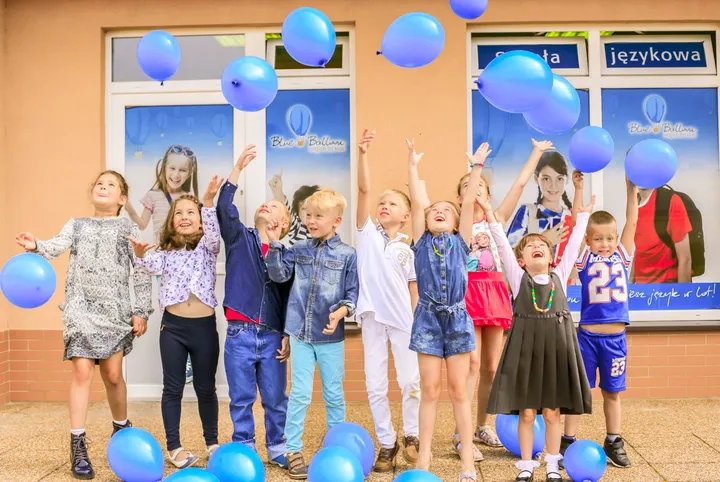 Grupa dzieci z niebieskimi balonami przed wejściem do szkoły Blue Balloon