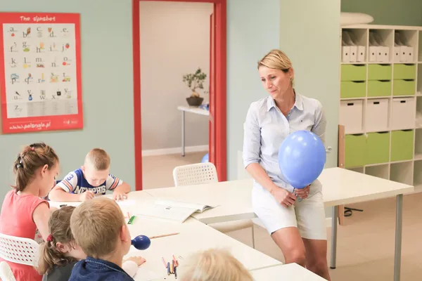 Nauczycielka siedzi przy dzieciach i pracuje z nimi nad materiałami do lekcji