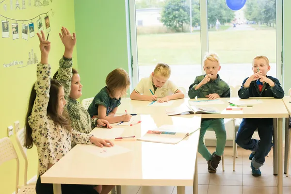 Dzieci siedzą przy stole i podnoszą ręce podczas lekcji