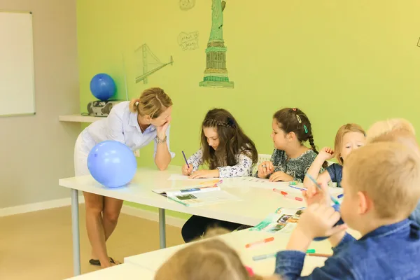 Dzieci pracują przy stole, a w sali widać niebieskie balony