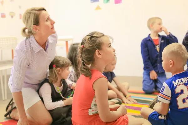 Lektor siedzi z grupą dzieci podczas zajęć na dywanie