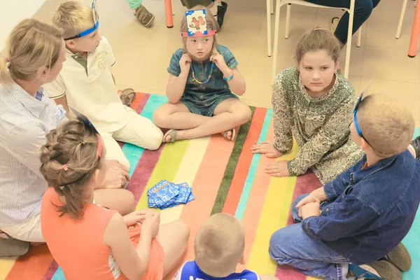 Dzieci siedzą na dywanie i biorą udział w zabawie edukacyjnej