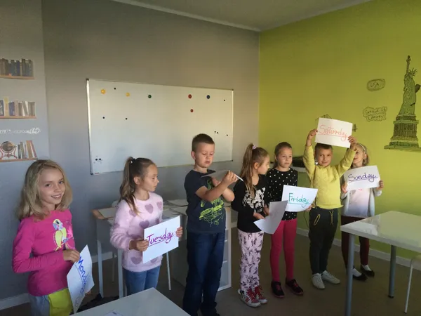 Grupa dzieci stoi w sali lekcyjnej i pokazuje swoje prace