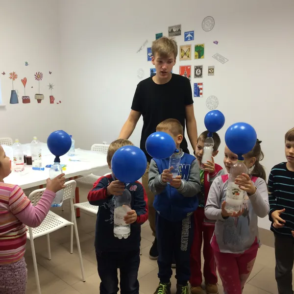 Lektor stoi z grupą dzieci trzymających niebieskie balony w sali lekcyjnej